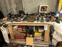 Wide view of wooden workshop bench with assortment of hand tools on top and storage underneath including cans, boxes, and small parts.