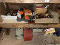 Overview of assorted hand tools in cardboard boxes and toolboxes on wooden shelf