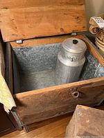 Vintage aluminum milk can inside one wooden dairy delivery box with aluminum lining, showing weathered interior and lid open.