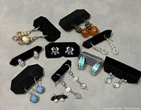 Eight pairs of various sterling silver earrings displayed on black earring cards.
