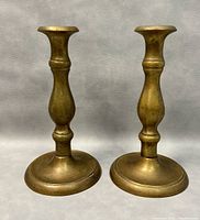 Front and side views of two solid brass antique candlestick holders showing their shape, size, and patina.