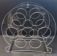 Front view of the clear Lucite acrylic circular wine rack showing the various circular holes for holding wine bottles and the GE logo on the stand base.