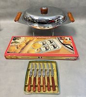 Photo showing all items in the lot: the covered serving dish with Bakelite handles, boxed ravioli mould, and box of six butter spreaders with Bakelite handles.