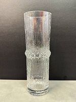 Front view of a clear textured glass vase showing vertical ridges and bubble band texture, standing against dark background.