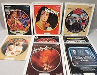 Twelve RCA SelectaVision CED videodiscs displayed in their original cardboard sleeves, showing a mix of movie covers including Rocky, MASH, Apocalypse Now, Papillon, and others.
