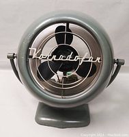 Front view of the vintage Vornado fan showing the chrome grille with 'Vornadofan' script logo and three black blades inside a round gray body.