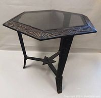 Angle view of the octagonal metal frame with floral detailing, glass inset, and one leg visible.