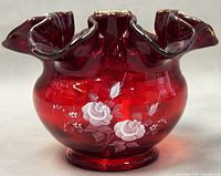 Front view of the ruby red scalloped glass bowl with white hand painted roses and floral design, gold trimmed edge.