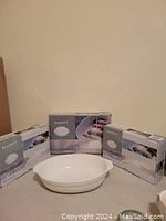 Three boxed Berghoff Bianco white oval ceramic casserole dish sets with one unboxed dish in front