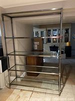 Full front view of the chrome and glass stand showing the five glass shelves and metal frame.