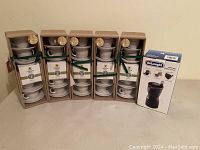 Five Starbucks espresso cup sets boxed with white cups, saucers, and small coffee packs, along with a boxed DeLonghi coffee grinder.