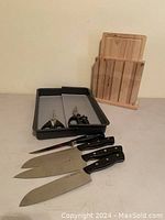 Four Zwilling Henckels kitchen knives alongside a wooden knife block and a tray holding two pairs of scissors.