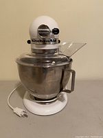 Front view of white stand mixer with stainless steel bowl and pour shield