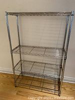 Full view of the metal wire shelving unit showing four shelves on a wooden floor against a wall.