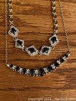 Close-up image of the necklace and bracelet laid on wood surface, highlighting the black stones and silver chain details.