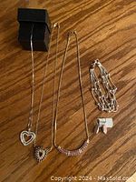 All jewelry pieces displayed together on wood surface; shows three necklaces with heart pendants, bracelet, and earrings with tag.