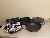 Front view of all pans including round frying pans, divided grill pans, and glass lid