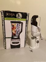 Ninja Professional blender in damaged box alongside corded hand blender with stand, mixing cup, and extra blade.