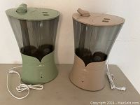 Pair of humidifiers, one green and one beige, shown side by side with power cords visible.