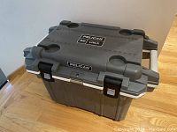 Cooler closed on wooden floor showing grey lid, latches and handles.