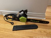 Full view of Poulan electric chainsaw with protective bar cover placed on the floor.