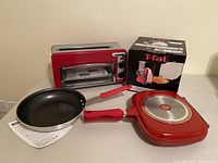 Red Hamilton Beach toaster oven, T-fal double grill pan with box, and red frying pan with instructions.