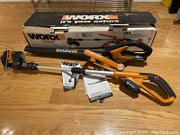 Two Worx cordless yardwork tools, one blower and one trimmer, with manuals and original box on wooden floor.