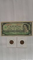 Front side of Canadian Centennial one dollar banknote featuring Queen Elizabeth II and two Canadian pennies in holders