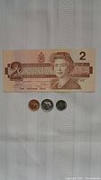 Canadian $2 banknote featuring Queen Elizabeth II and three coins laid below it.