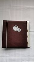 Closed brown coin album with silver accent stripe and coin embossing on cover.