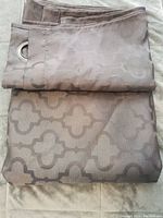 Folded light brown curtain with geometric pattern visible, showing silver metal grommet