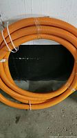 Coiled bright orange expandable hose against a wall and floor surface.
