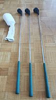 Three wooden head golf clubs with green grips alongside white knit headcover