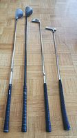 Four right-handed golf clubs including driver, two woods, iron, and putter seen on wooden floor