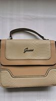Close-up view of Guess handbag front showing textured snake-skin pattern, tan accents, and silver Guess logo.