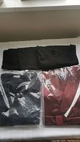 Folded black cardigan sweater, three black t-shirts, and packaged maroon men's house robe