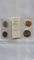 Photo showing four coins from the 1964 South Arabia mint set, sealed in plastic with a description card in the center.
