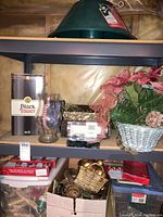 Shelf with green plastic Christmas tree stand on top shelf, Black Tower candle box, glass candle holder, floral arrangement, and multiple baskets and trays of ornaments and decorations.