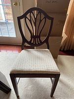 Front view of a single shield back dining chair with padded beige cloth seat, showing the wooden frame and fabric detail.