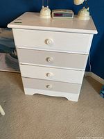 Front view of the entire white four drawer dresser with rounded knob handles on drawers, showing condition and structure.
