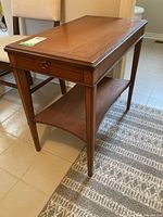 Wooden end table with pull-out tray from a front angle, showing the top, legs and lower shelf with some scratches visible.