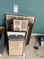 Assortment of empty photo frames stacked and leaning against a wall, showcasing variety in frame sizes and finishes.