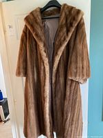Full length view of brown mink fur coat hanging on a hanger, showing overall shape and length.