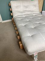Side view of the futon mattress and wooden frame showing white tufted mattress on the slatted wooden frame.