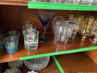 Shelf showing blue tinted glasses with gold floral decoration, Finlandia Vodka shot glasses, and clear brandy glasses.