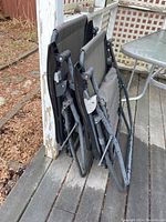 Two folded outdoor gravity chairs leaning against a post on a wooden deck, showing rust on frame and mesh fabric seats.