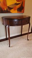 Front view of vintage wood hall table with curved legs and two drawers, showing overall structure and finish.
