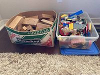 Cardboard box filled with wooden blocks and plastic bin with assorted LEGO pieces