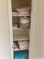 Closet shelves with neatly folded bed linens including sheets and pillowcases in white, pink, and gray.