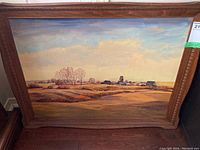 Full view of framed oil painting showing rural landscape with fields, trees, buildings, and sky.